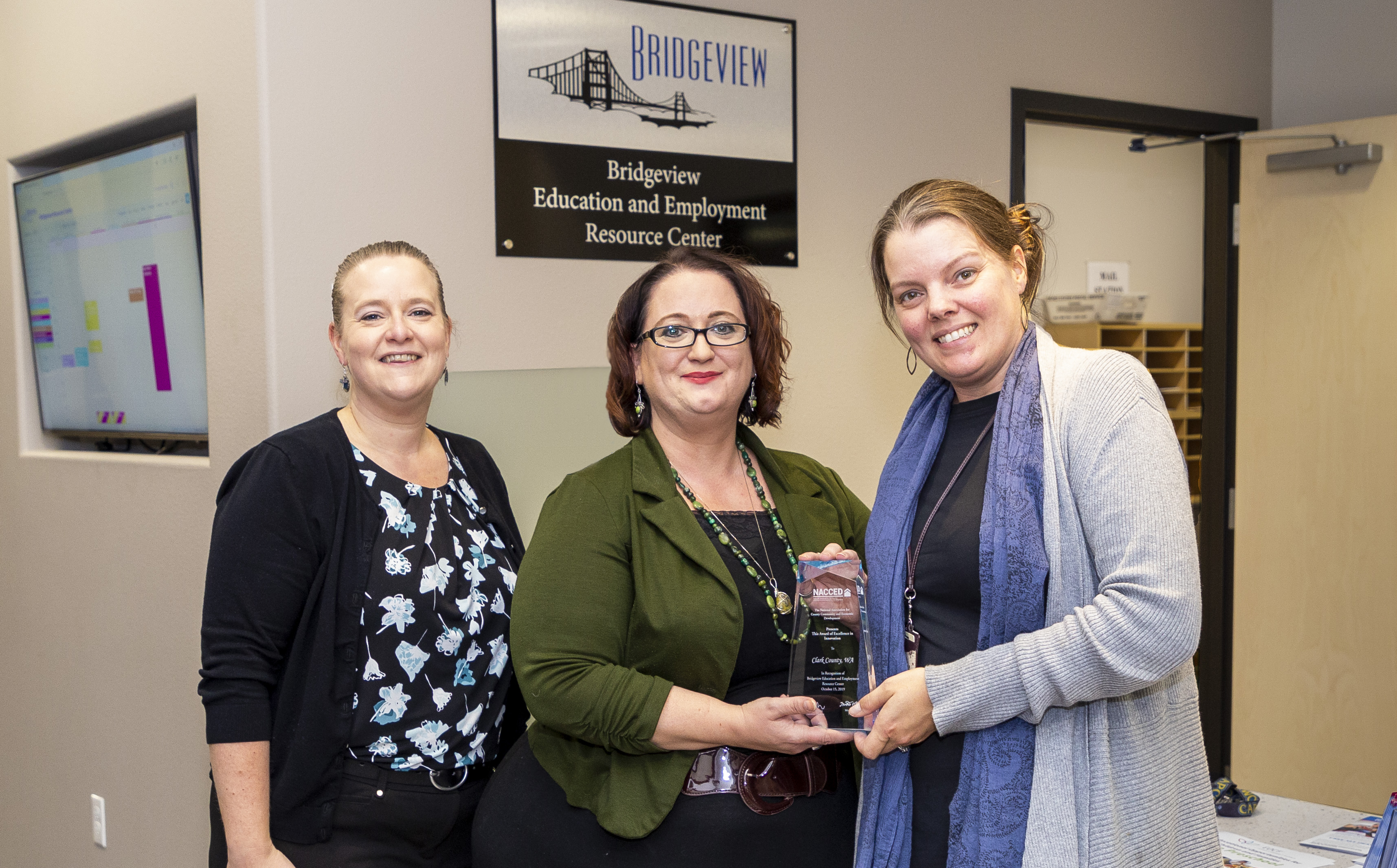 The National Association for Community and Economic Development (NACCED) recently recognized Bridgeview Resource Center with its Award of Excellence in Innovation. Clark County Community Services Program Coordinators Rebecca Royce (left) and Samantha Whitley (right) present the award to Bridgeview Executive Director Angie Sytsma (center).