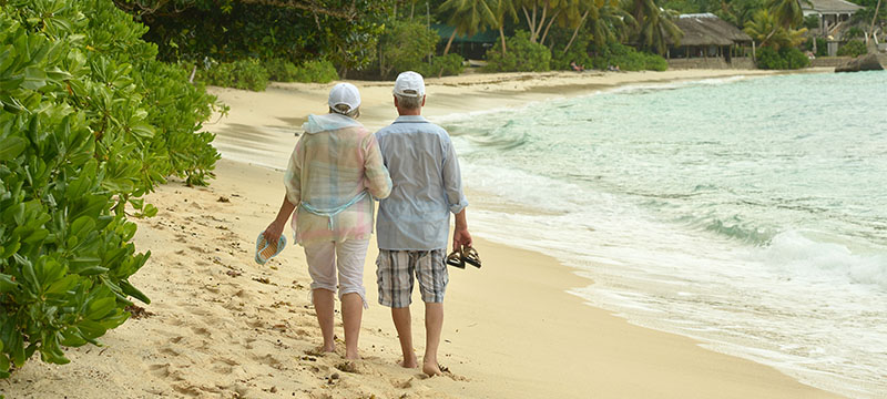 Older white couple walking on a tropical beach
