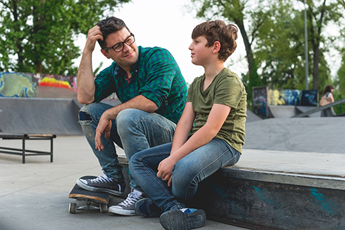 White adult male talking to his son at a skateboard park