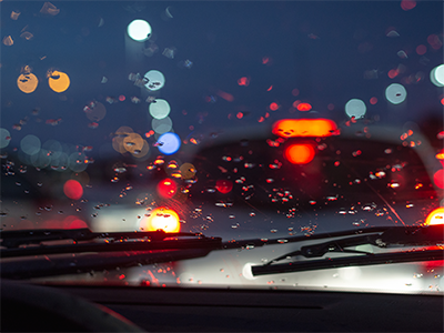 Dashboard of a car looking out the front windshield on a rainy evening.