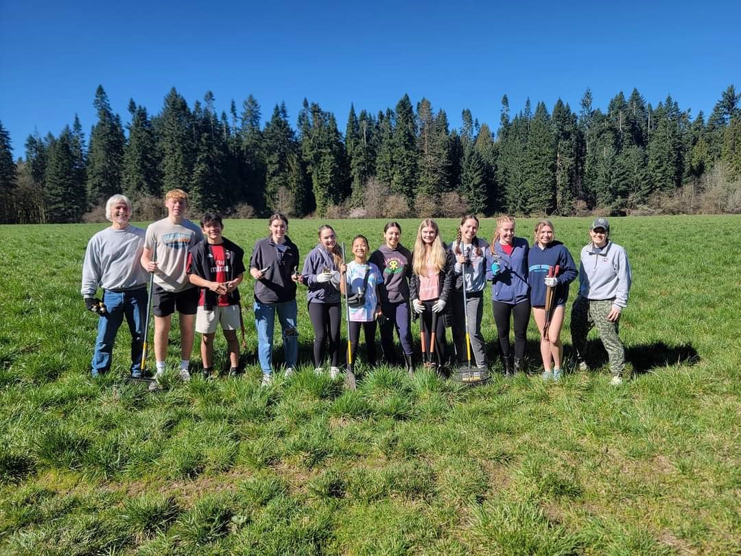 12 volunteers standing with rakes in an green field