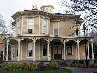 Front view of historic Slocum House. Tan Victorian style home with cream trim. Features a front porch that wraps around the side of the building.