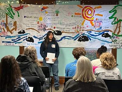 Participants at Clark County Youth House listen to a student presentation. Presenter is standing front a mural created by the group.