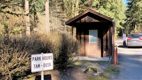 Small wood booth in the foreground, vehicle at a parking meter in the background, in a forested setting