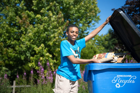 Boy putting carboard in blue recycling cart
