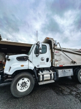 A large white truck with dumper bed in front of a cloudy sky. 