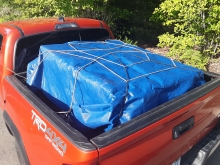 Red 4x4 pickup truck with a full load secured by a blue tarp and ropes. 